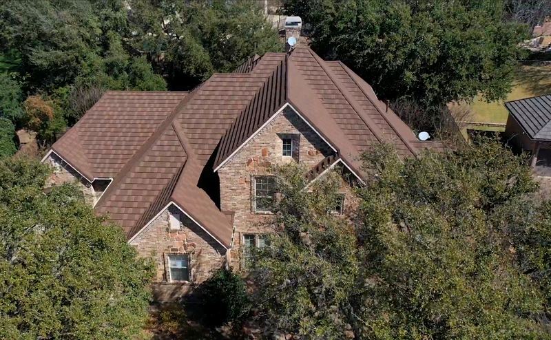 Aerial view of a stone home with a brown metal shingle roof by Benchmark Roofing and Construction