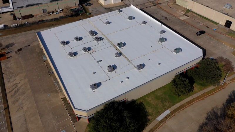 Aerial view of a commercial warehouse with a new white flat roof by Benchmark Roofing and Construction