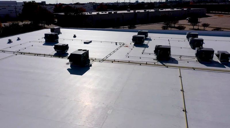 Aerial view of a commercial building with a new white TPO flat roof by Benchmark Roofing and Construction